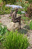 Bronze statue of young boy sitting on rock in gravel area of John Masseys Garden, Ashwood, West Midlands