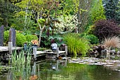 Pond area with decking silver spheres and grey slate plinths mature shrubs and trees in May Late Spring