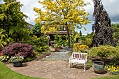 Colourful mature shrubs and trees dovecote white bench in May late Spring in John Massey`s Garden Ashwood