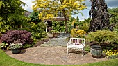 Colourful mature shrubs and trees dovecote white bench in May late Spring in John Massey`s Garden Ashwood (NGS) West Midlands