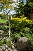 Model dovecote on gravel area large stone mature trees and shrubs in June Early Summer Ashwood (NGS) West Midlands