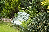 White metal bench in mature garden