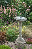 A plant lovers cottage garden colour combinations of pink roses and penstemon with deep purple geranium around sun-dial at Coley Cottage (NGS) Little Haywood, Staffordshire