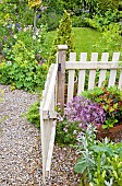 Open pale cream wooden garden gate, borders of summer flowering herbaceous perennials