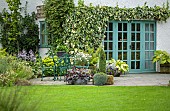 Patio area green wrought iron table and chairs with views across lawns to borders