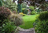 Garden view from gravel path to wooden garden shed sweeping borders