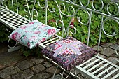 Seating area in garden, lovely flowered cushions on white iron ornate bench