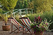 Monet Bridge over lake, brightly coloured stripped deck chairs on gravel area at Wilkins Pleck (NGS) 6 acre Country Garden with garden rooms and Aboretum at Whitmore near Newcastle-under-Lyme in North Staffordshire