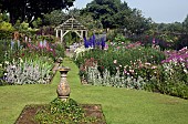 Stone sundial in lawn with twin borders of herbaceaous perennials