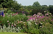 Border of herbaceous perennials, brick walls surrounded by mature trees