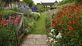 An Arts and Crafts oak gate opens to long grass path with borders either side of herbaceous perrenials