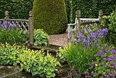 Terraced seating area, with Alchemilla mollis ladys mantle with blue Iris against oak fencing