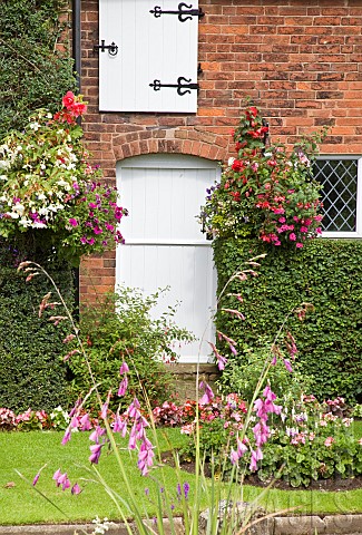 Front_of_cottage_with_well_planted_hanging_baskets_mature_shrubs_lawn_and_borders