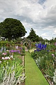 Stone sundial in lawn with twin borders of many varieties of herbaceous perrenials