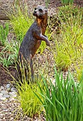 Bronze otter on gravel area with grasses in May Late Spring in John Massey`s Garden Ashwood (NGS) West Midlands