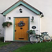 Front garden porch with wooden door hanging basket and wreath also floral displays in containers on an old pushbike