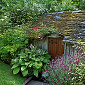 Boathouse in summer with herbaceous perennials, mature trees and shrubs