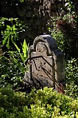 AN ANCIENT STONE WATER FEATURE AMONG GARDEN PLANTING