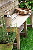 WOODEN BENCH WITH WICKER BASKET AND WATERING CAN.
