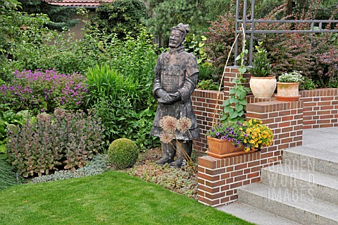 PERENNIAL_BORDER_WITH_POTTED_PLANTS_AND_REPRODUCTION_OF_A_CHINESE_CLAY_WARRIOR