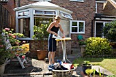 MIDDLE AGED FEMALE DOING THE IRONING IN HER GARDEN ON A HOT SUNNY DAY. MODEL RELEASED