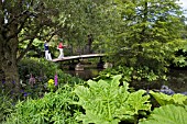 VISITORS CROSS THE BRIDGE AT THE LOWER POND IN THE  RHS GARDEN  HYDE HALL.