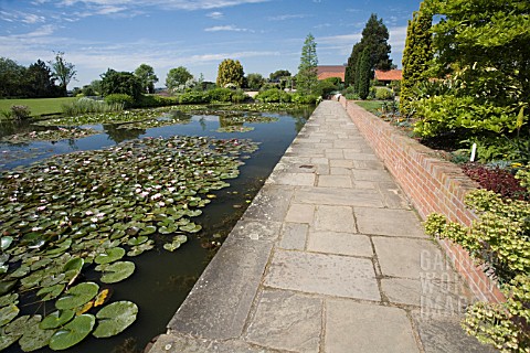 THE_TOP_POND_AT_RHS_GARDEN__HYDE_HALL_WITH_A_PATH_AND_LOW_WALL_RUNNING_ALONG_SIDE_THE_WATER