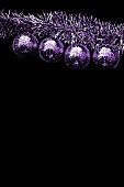 FOUR PURPLE MAUVE CHRISTMAS BALLS HANGING AGAINST A BLACK BACKGROUND